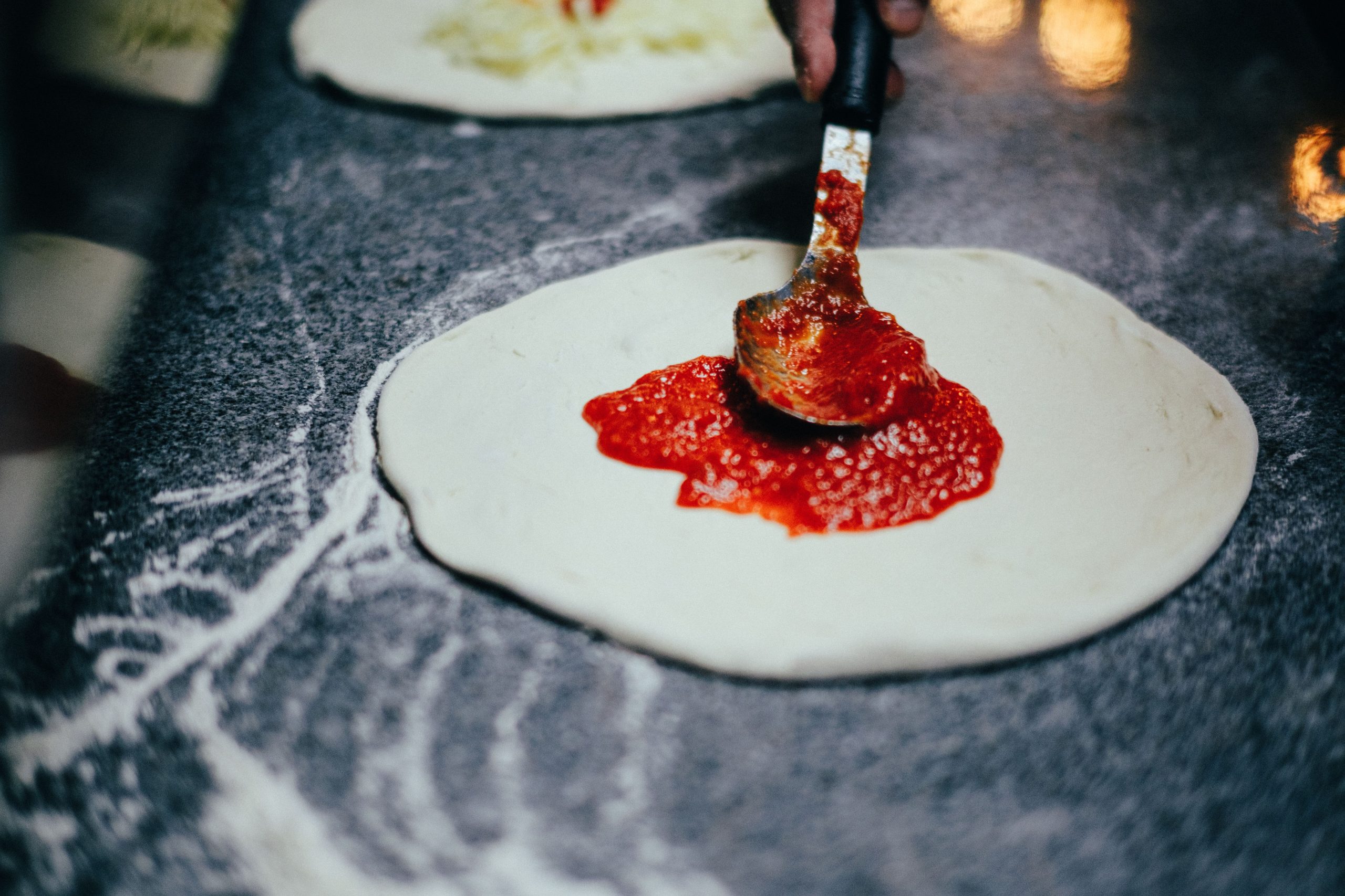 Close-up of a brush spreading savory sauce onto dough