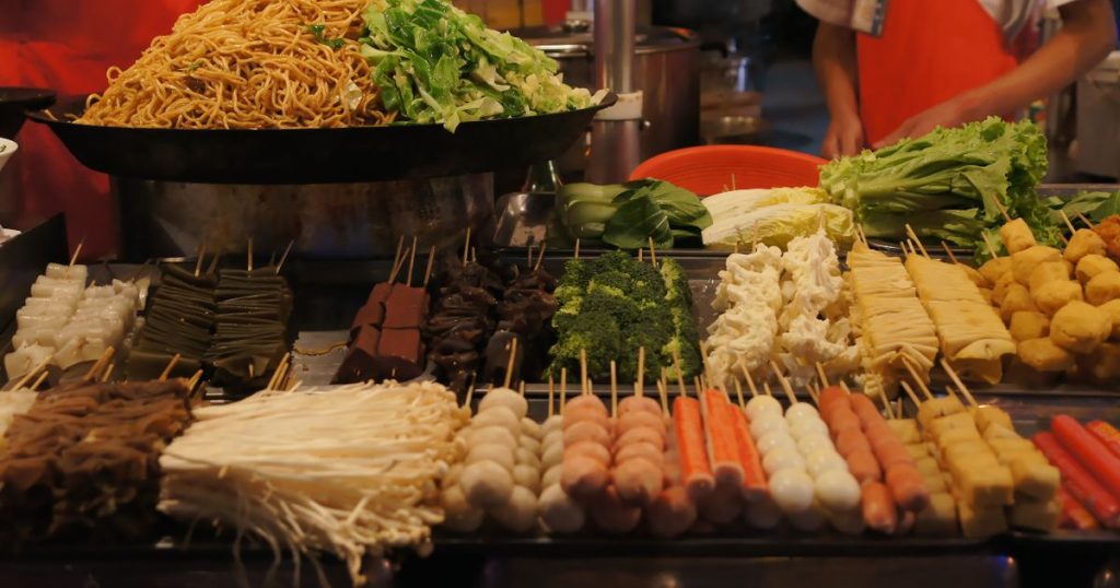 Colorful Asian street food display with skewers and fresh vegetables under warm market lighting