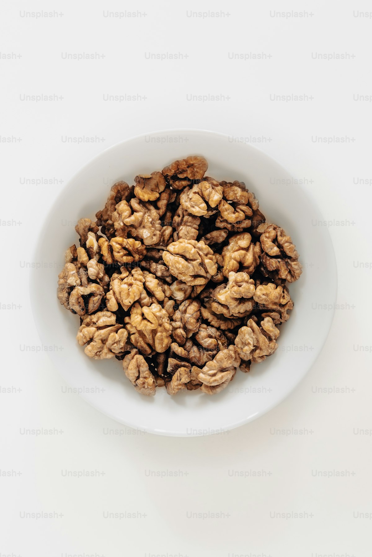 A white bowl filled with whole walnuts on a wooden table