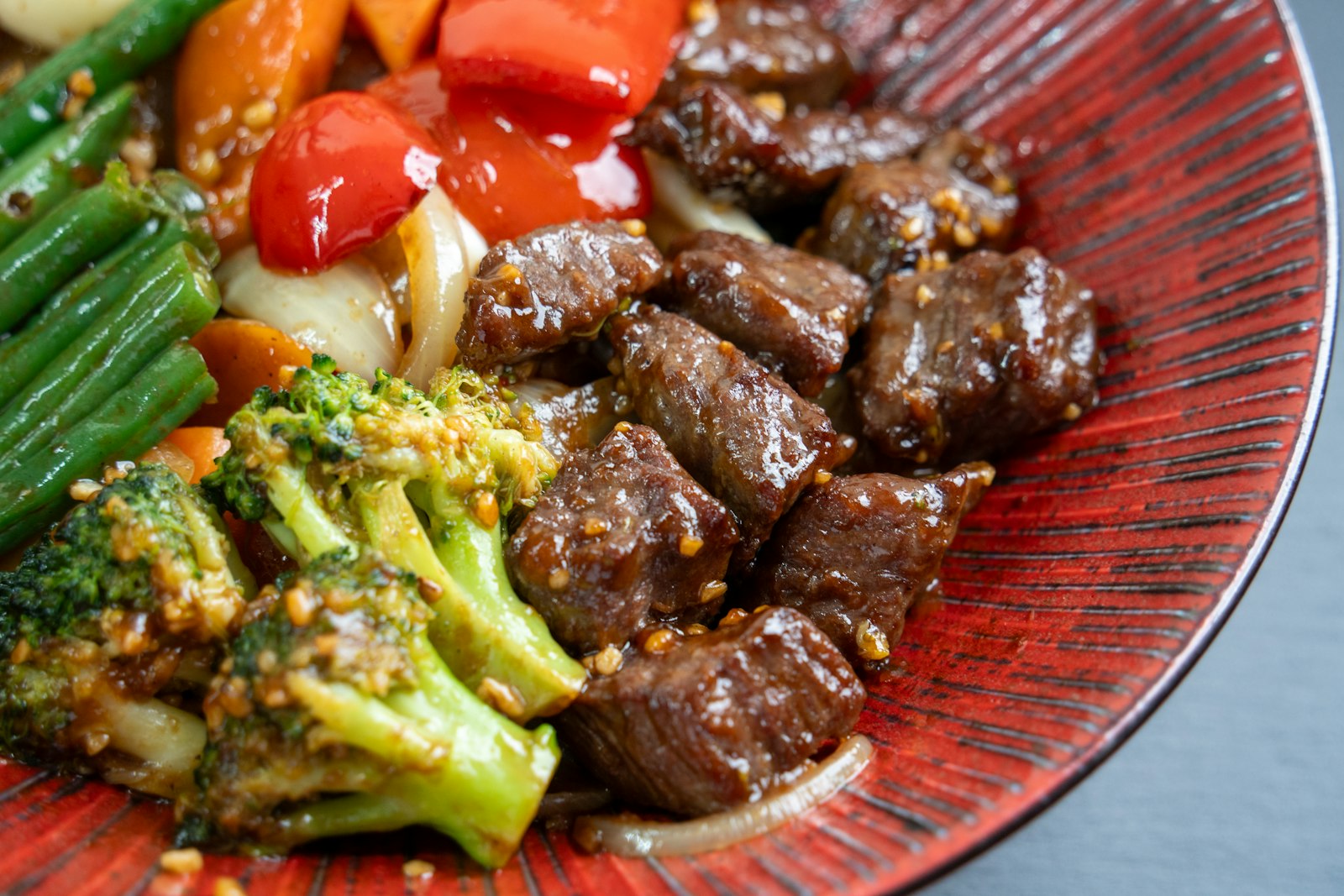 Beef and broccoli stir fry with vegetables on a red plate