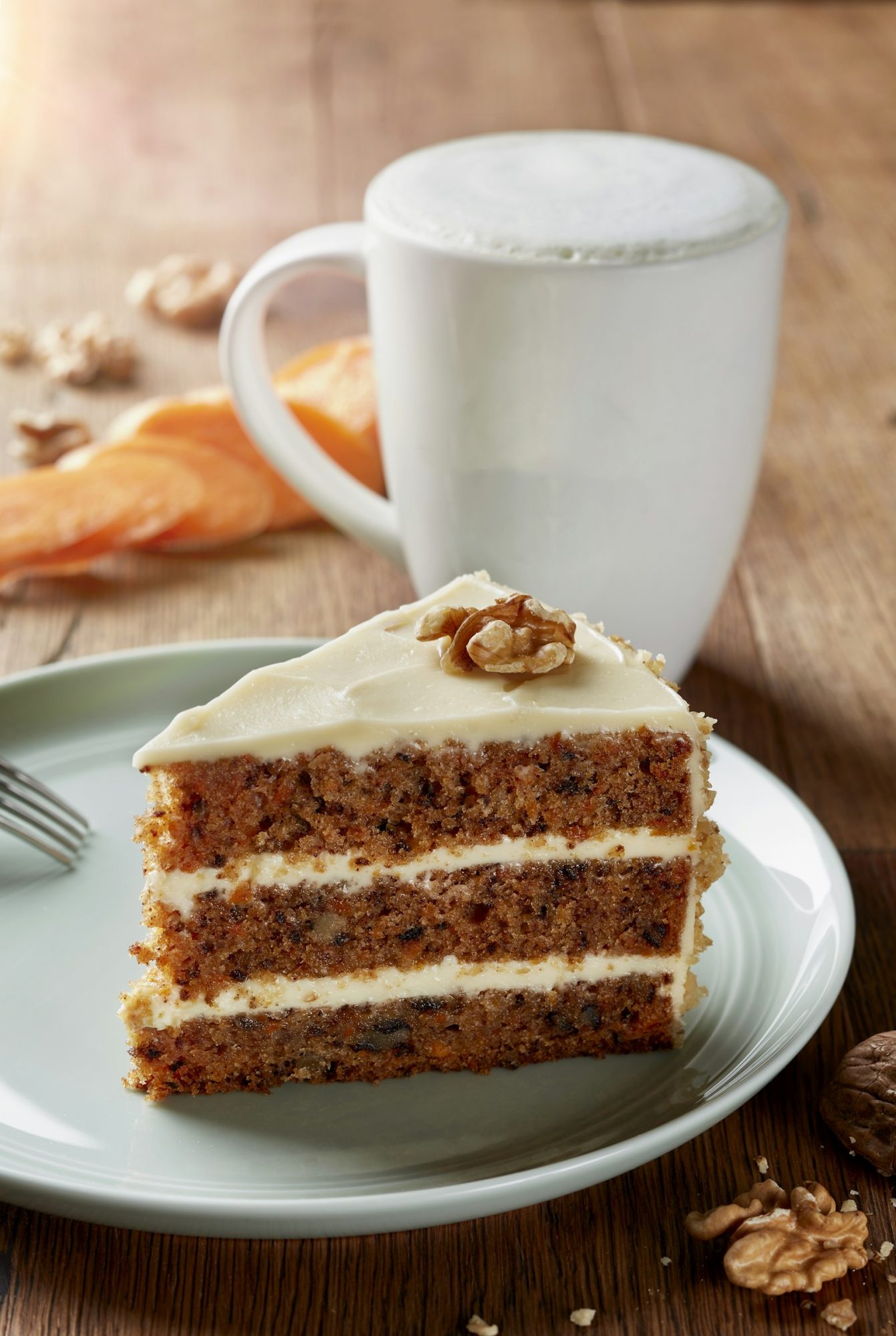 Slice of three-layer carrot cake with cream cheese frosting and walnuts