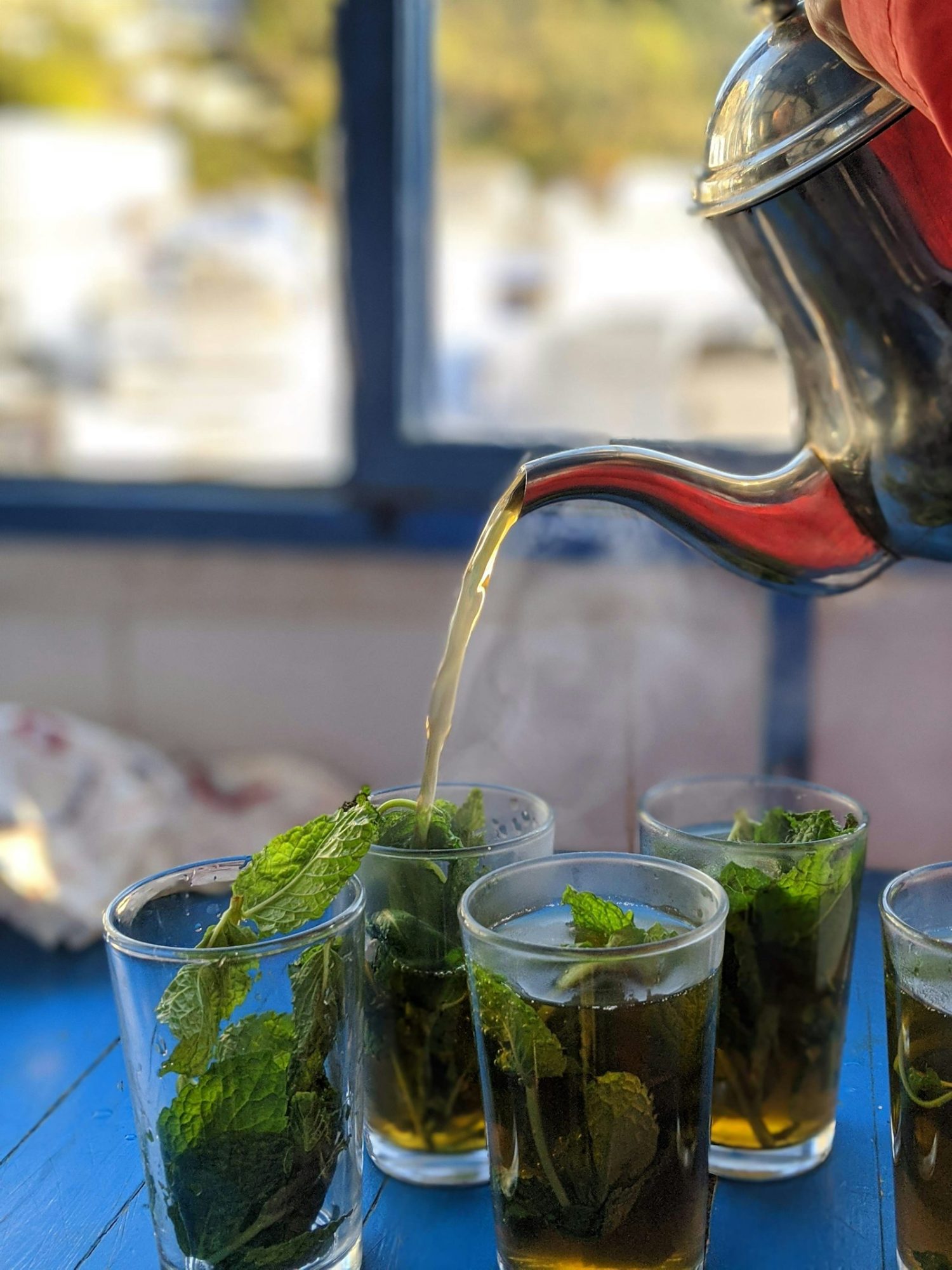 Moroccan mint tea poured from a silver teapot into glasses with fresh mint
