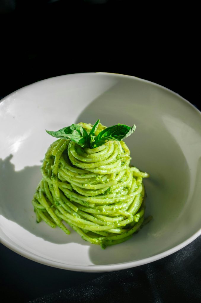 Pesto pasta twirled on a white plate with fresh basil